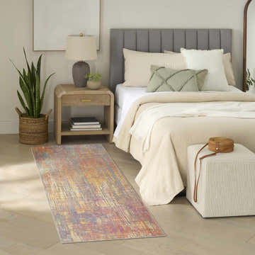 Bedroom scene with Nourison Botanical Multicolor rug, wood floors, neutral bedding, and a woven ottoman.