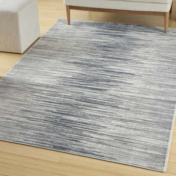 Modern living room scene with a grey Nourison Home Texture area rug, white chair and ottoman on wood floor.