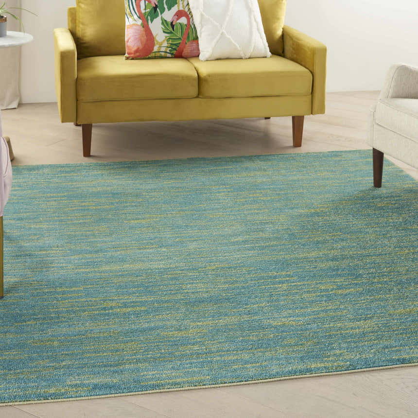 Living room scene with a Nourison Essentials Blue Green Outdoor Area Rug, yellow loveseat, and light wood floors.