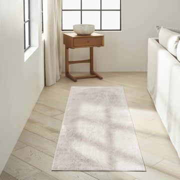 Modern living room with Calvin Klein CK024 Irradiant Silver Gray rug, wood floors, side table, and white sofa.