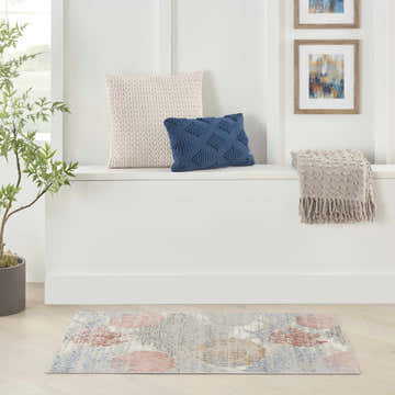 Coastal room scene with Nourison Seaside Multicolor rug, bench with pillows and blanket, and framed art.
