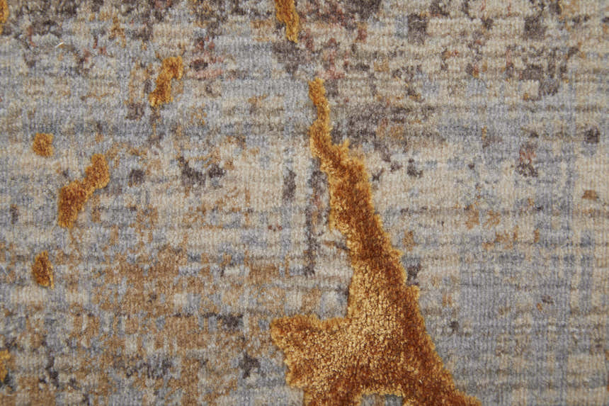 Close-up of the Feizy Pryor rug showing its abstract gold design on a gray and brown textured background. Texture
