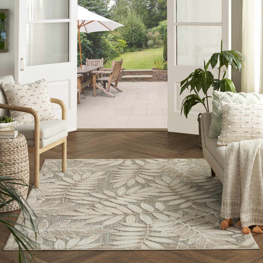 Living room with Nourison Aloha Natural Tropical Area Rug, herringbone wood floors, and open doors to a patio.