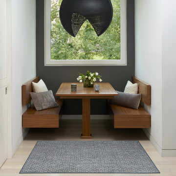 Dining nook featuring a Nourison Tulum Denim Outdoor Area Rug, wood benches, table, and a view to the outside.