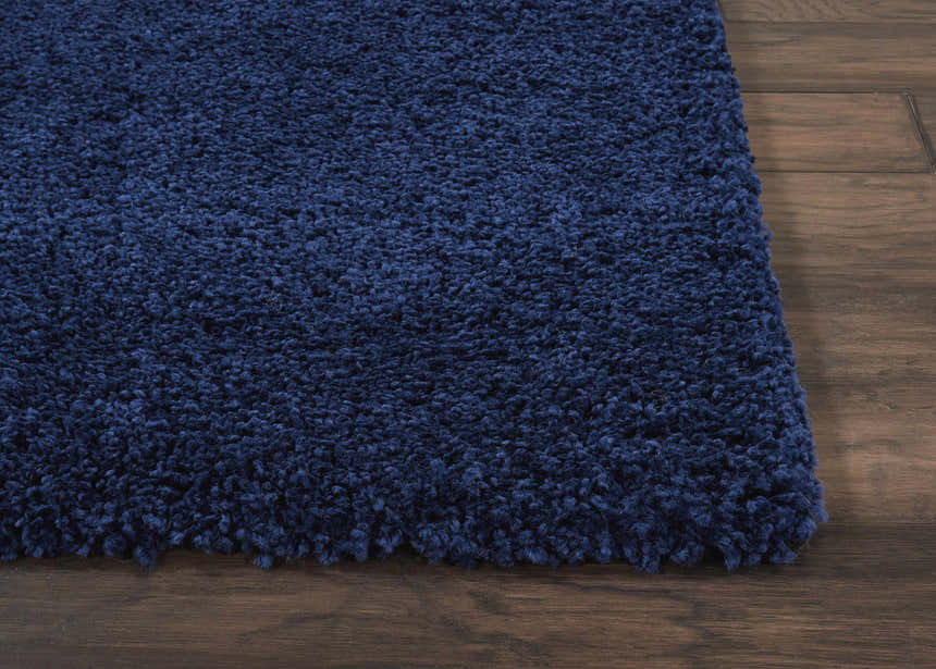 Close-up of the plush, textured Nourison Malibu Shag Navy rug on a dark hardwood floor.