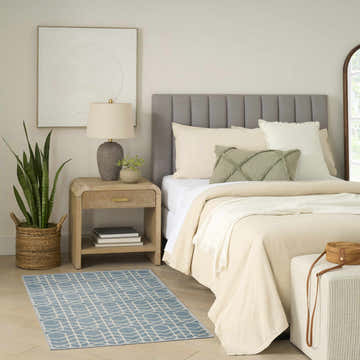 Serene bedroom with a Nourison Charm Blue Ivory rug, wood nightstand, snake plant, and neutral bedding.