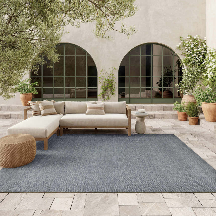 Denim Nourison Tulum outdoor rug on a patio with a sectional sofa, plants, and neutral tones.