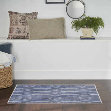 Bathroom scene with Nourison New Concept Navy rug, dark wood floors, white walls, and decorative pillows and plants.
