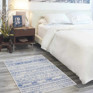 Bedroom scene with a Nourison Whimsicle Ivory Blue rug. The rug has a bohemian pattern and is placed on gray wood floors.