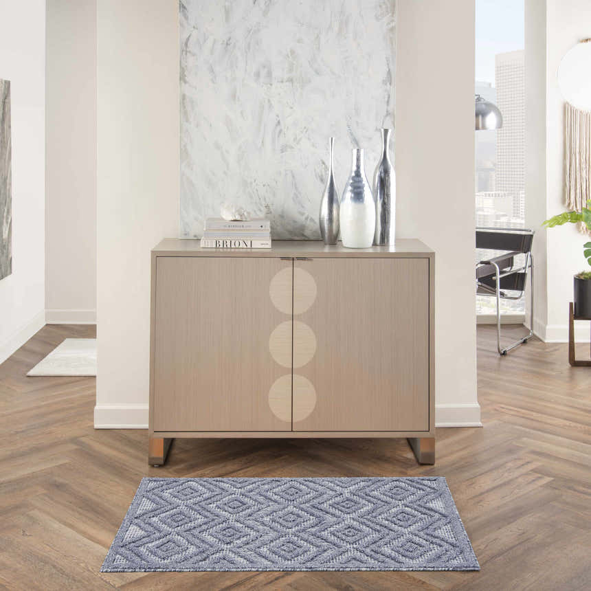 Entryway scene with a Nourison Versatile Denim Blue rug, wood floors, and modern cabinet with silver vases.