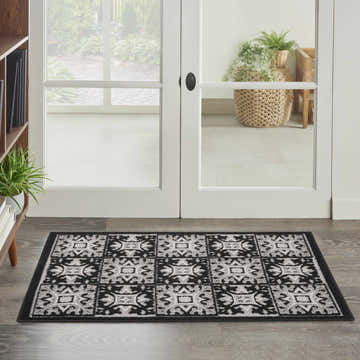 Entryway scene with a Nourison Aloha Black White Contemporary Area Rug on wood floors near a white door.