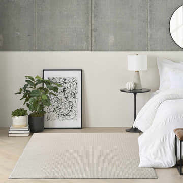 Modern bedroom scene with a beige DKNY Atlantic Avenue rug, white bedding, and minimalist decor.