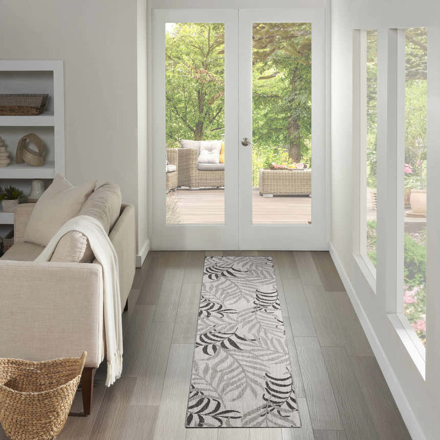 Living room scene with a Nourison Garden Oasis Grey Tropical Area Rug runner leading to an outdoor patio.