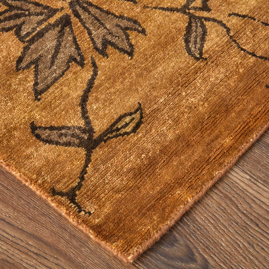 Close-up of Feizy Cordonnet rug showing brown floral pattern on orange wool with hand-knotted texture. Corner