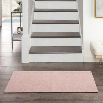 Entryway scene with a Nourison Essentials Pink Outdoor Area Rug on dark wood floors near stairs.