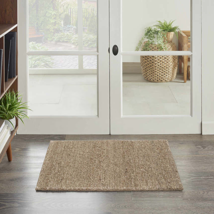 Entryway scene with a beige Nourison Alanna area rug on gray wood floors, white french doors, and a glimpse of the garden.