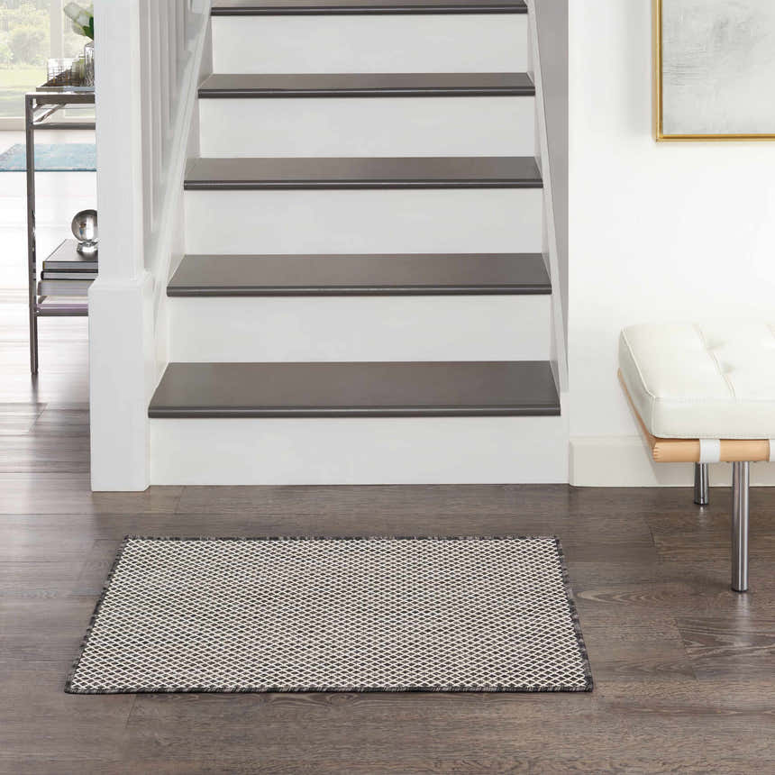 Entryway scene with a Nourison Courtyard Ivory Charcoal rug, dark wood floors, white stairs, and a white leather bench.