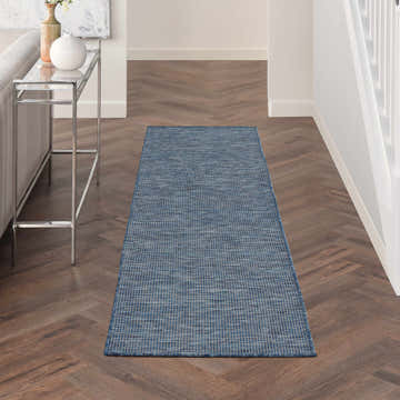 Hallway scene with a Nourison Positano Navy Blue runner rug on herringbone wood floors. Modern decor.