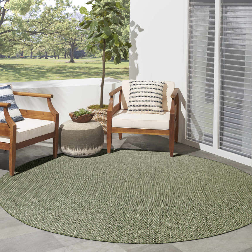 Outdoor patio scene with a round green Nourison Horizon area rug, chairs, and a tree.