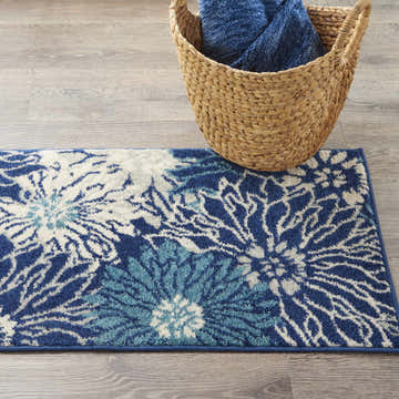 Close-up of Nourison Passion Navy Ivory rug with floral design on wood floor next to a woven basket.