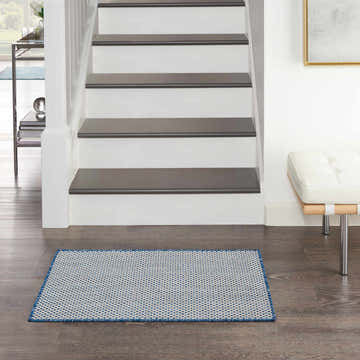 Entryway with stairs and Nourison Courtyard Ivory Blue Modern Area Rug. White walls, dark wood floors, and a white bench.