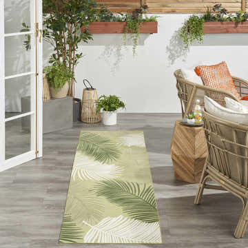 Suncoast Green Tropical Area Rug in a sunroom with rattan chairs and potted plants.