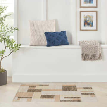 Modern room scene with beige multicolor Nourison Astra area rug, pillows, throw blanket, and framed art.