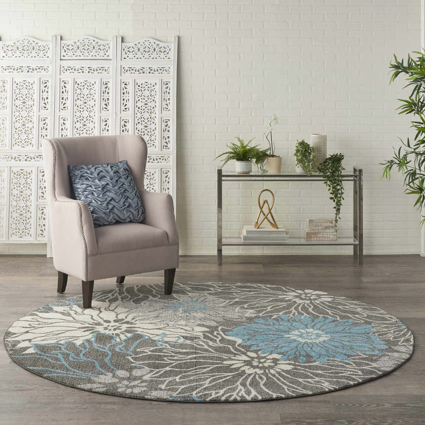 Living room scene with a round Nourison Passion Charcoal Blue rug, taupe chair, and white brick wall.