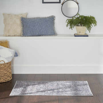 Bathroom scene with grey vintage Nourison New Concept rug on dark wood floor. White shelf with pillows, plant, and mirror.