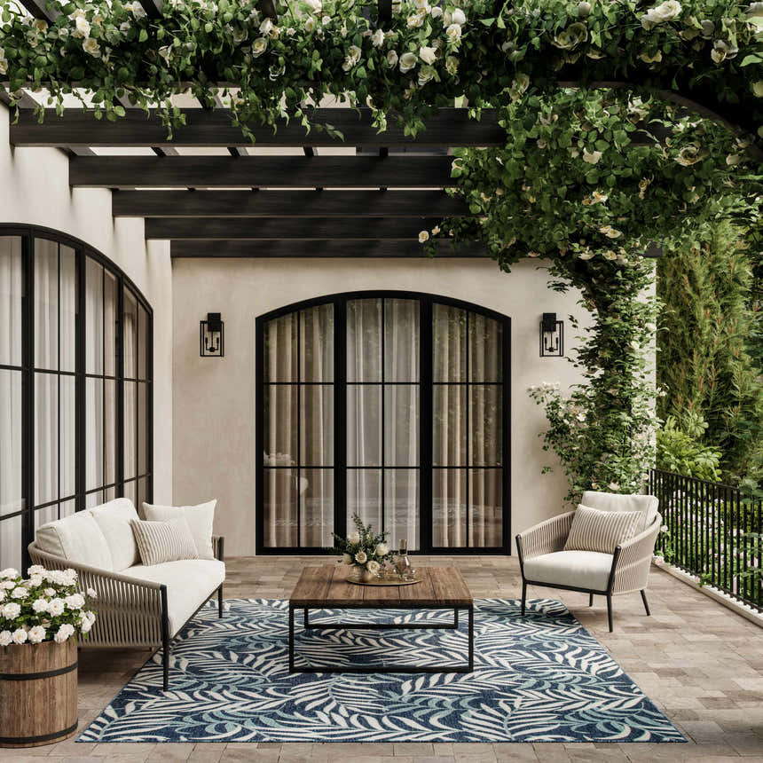 Outdoor patio scene with a Nourison Garden Oasis Navy Tropical Area Rug, white seating, and floral accents.