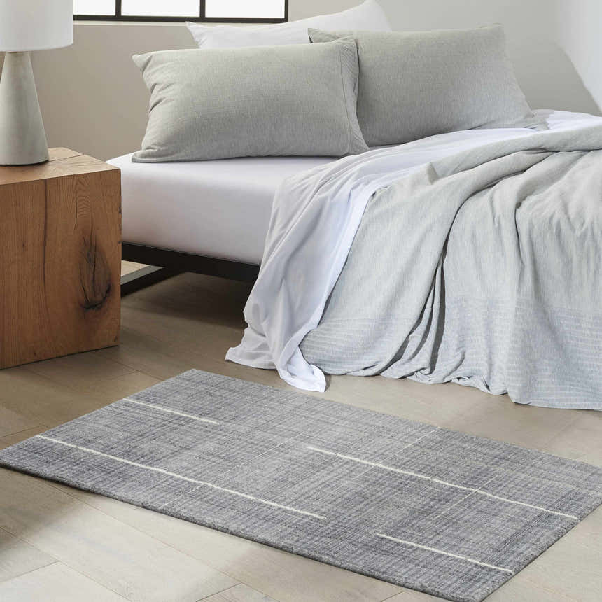 Serene bedroom scene with denim Calvin Klein CK041 Architectura area rug, wood nightstand, and gray bedding.
