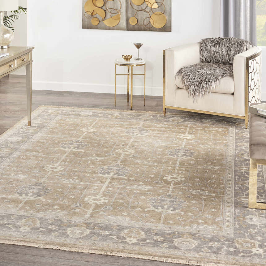 Living room scene with a Nourison Aldora Pewter vintage rug, cream chair, gold accents, and gray wood floors.