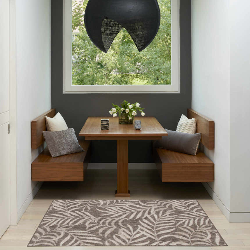 Breakfast nook with Nourison Garden Oasis Mocha Tropical Area Rug, wood table, and bench seating.