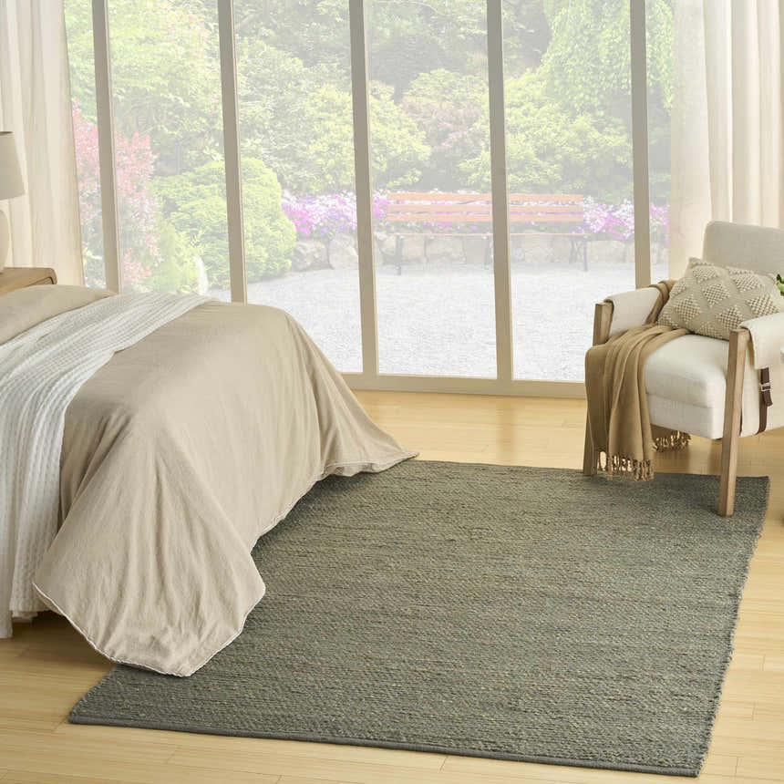 Bedroom scene with a muted sage Nourison Natural Jute rug, light wood floors, and garden view. Farmhouse style.