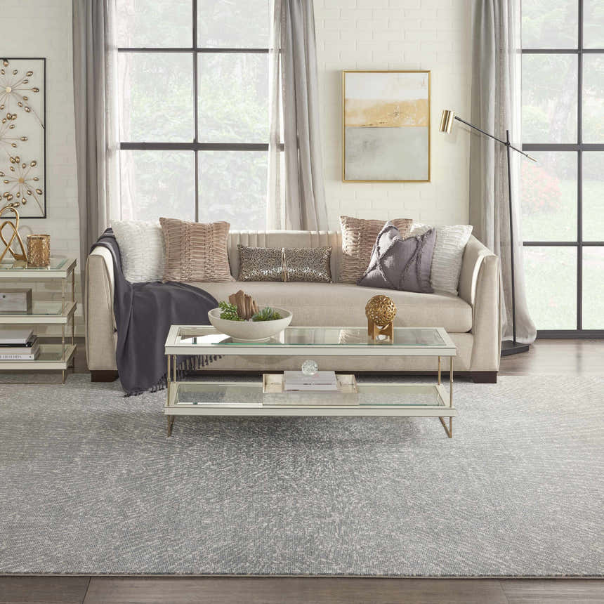 Living room scene with a grey Inspire Me! Home Decor Elegance area rug, sofa, glass coffee table, and natural light.