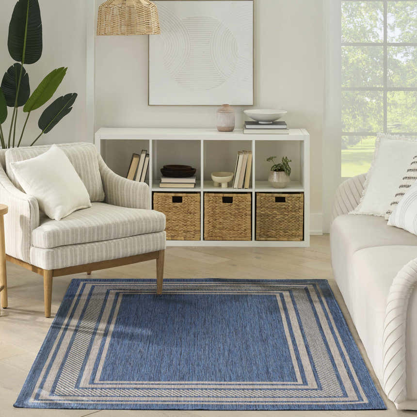 Living room scene with a blue Nourison Horizon Indoor/Outdoor Denim Modern Area Rug, neutral furniture, and natural light.