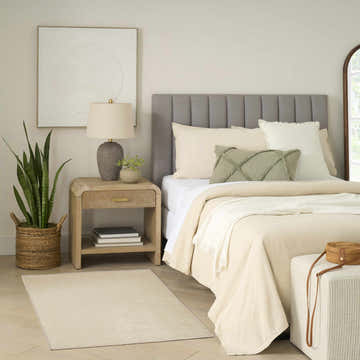 Neutral bedroom scene with the ivory Nourison Charm rug, wood nightstand, snake plant, and gray upholstered headboard.