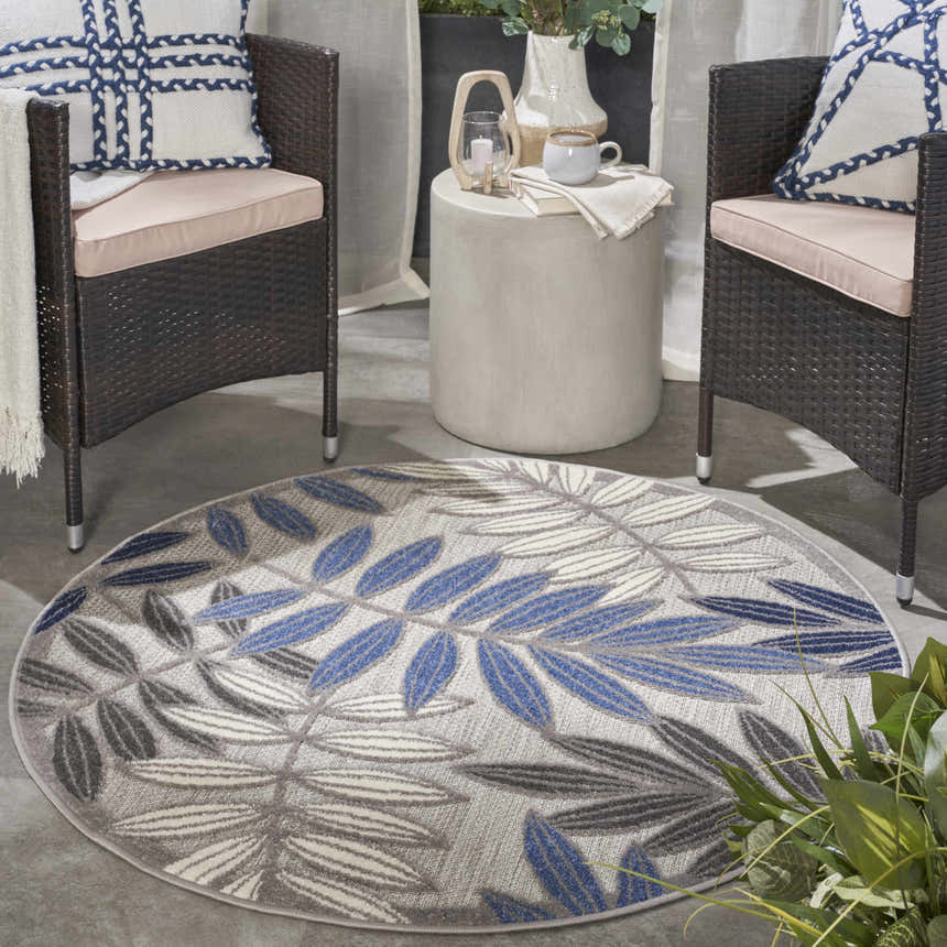 Patio scene with Nourison Aloha Grey Blue Tropical Area Rug, wicker chairs, and a small side table.