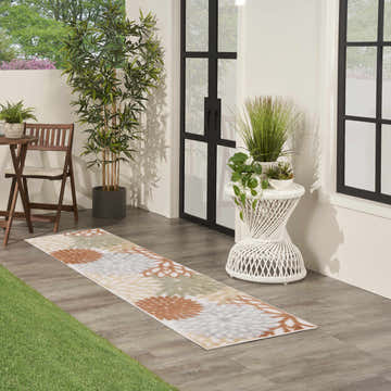 Outdoor patio scene with Nourison Aloha Ivory Multicolor rug, bistro set, and potted plants.