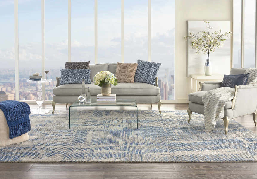 Light-filled living room with a Nourison Ellora Blue rug, gray sofa, glass table, and city view.