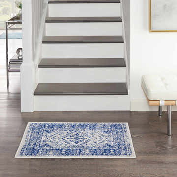 Entryway with Nourison Whimsicle Ivory Navy rug, dark wood floor, white stairs, and modern white bench.