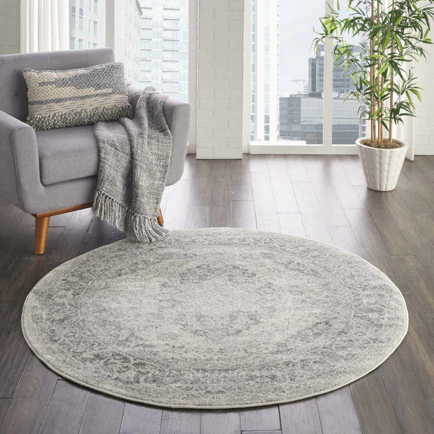 Living room scene with a round Nourison Tranquil Ivory Grey Vintage rug, grey chair, and city view.