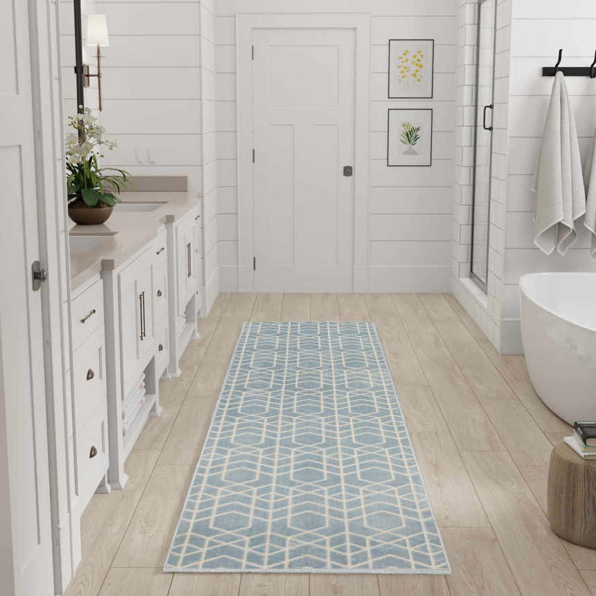 Bright bathroom scene with Nourison Charm Blue Ivory rug, white cabinets, wood floors, and modern geometric pattern.