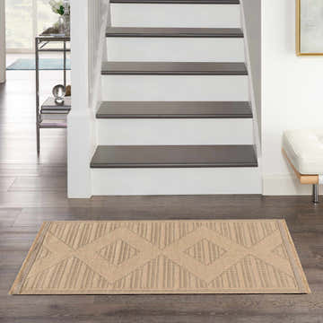 Entryway scene with Nourison Jute Natural Beige rug. Modern runner rug with geometric pattern on dark wood floor. Stairs in background.