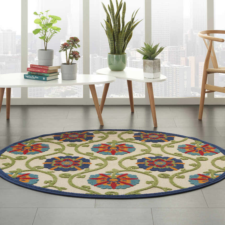 Modern living room with a round Nourison Aloha Blue Multicolor rug, plants, and city view.