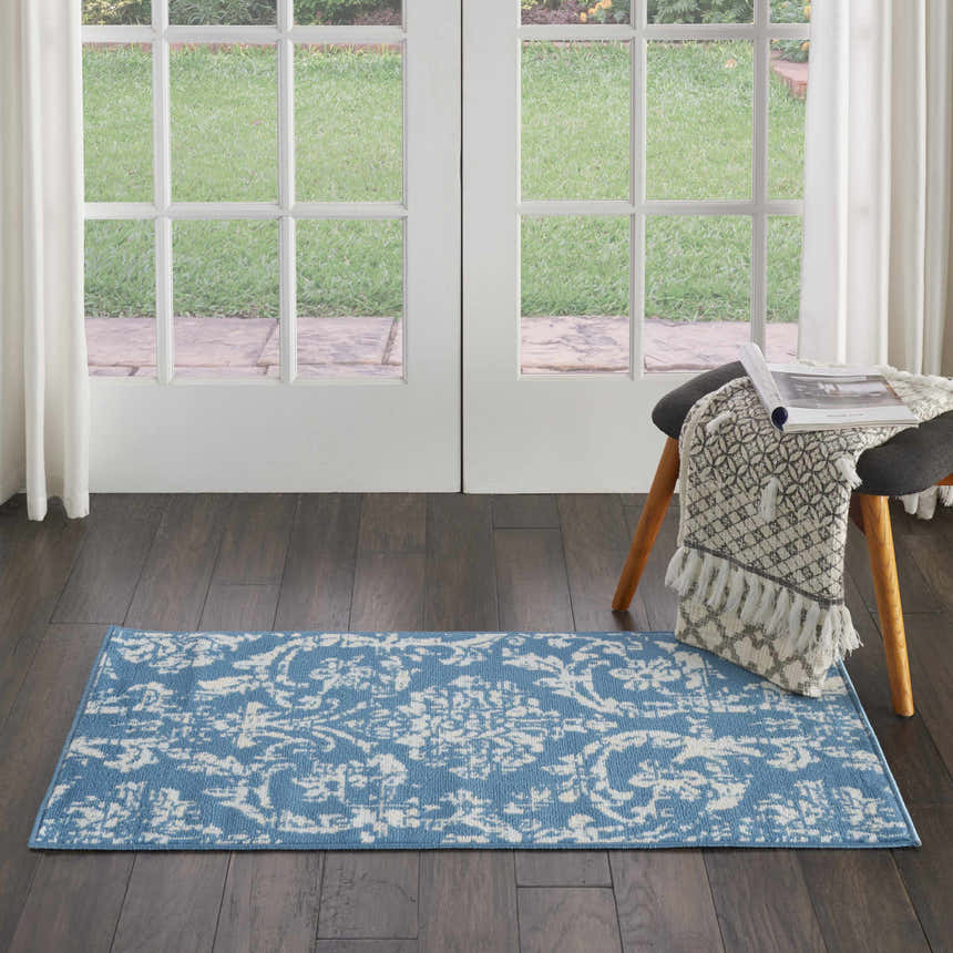 Light blue Nourison Jubilant Vintage rug runner on dark wood floor in front of a bright window. Stool with throw blanket.