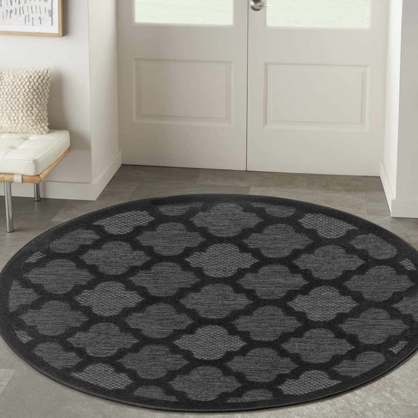 Entryway with a round Nourison Easy Care Charcoal Black rug, white door, and bench.