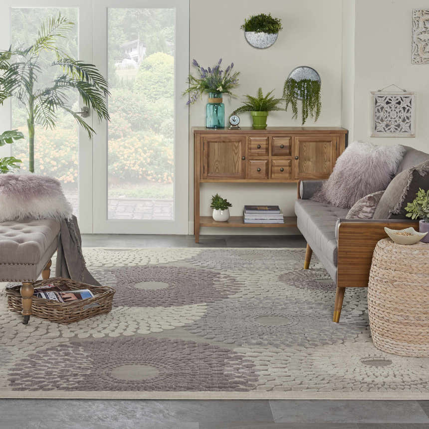 Living room scene with a grey sofa and the Nourison Graphic Illusions Grey Mid-Century Modern rug with a floral pattern.