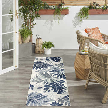 Outdoor patio scene with a Nourison Suncoast Blue Tropical runner rug, wicker chairs, and potted plants.