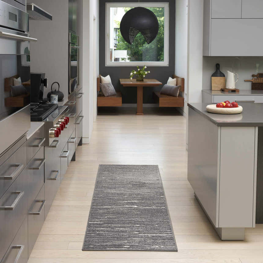 Modern kitchen with stainless steel appliances and Nourison Care Free Grey runner rug on light wood floors.